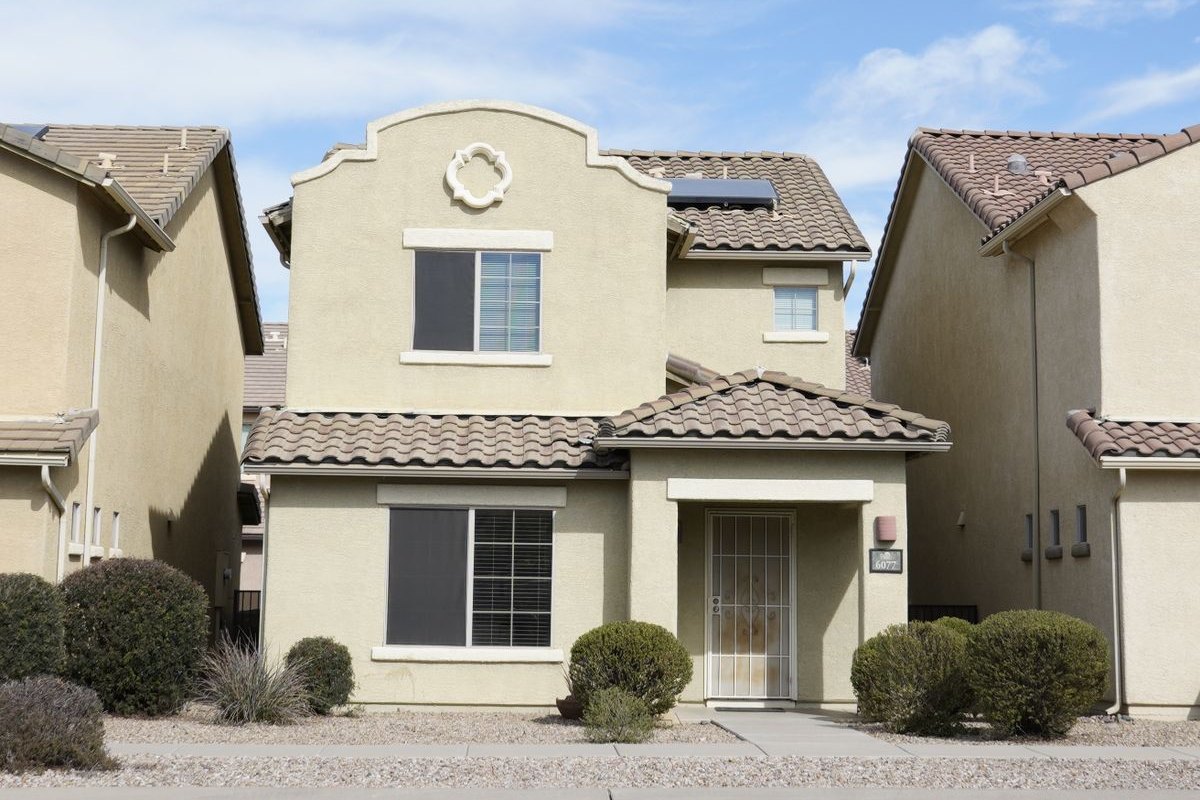 A two-story stucco tract home with a tile roof, security screen door and desert gravel landscaping on a clear day in the Southwest