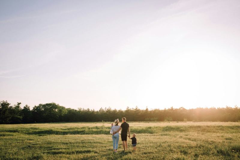 A young couple, one man and one woman, walking across open grassland with two small children at sunset